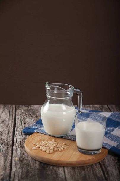 Vegetarian pine nut milk in a glass cup and jug, on a wooden stand with a blue linen napkin. - Foto, afbeelding