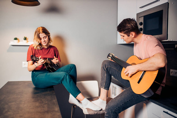 Kaukasischer Junge spielt Gitarre und Frau spielt Ukulele in Küche - Foto, Bild
