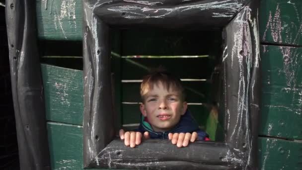 Chłopiec wygląda przez drewniane okno, grymas - Materiał filmowy, wideo