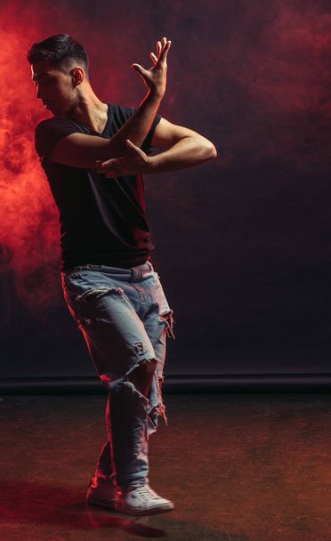 dancing pose of young man on the dark red smoky background - Φωτογραφία, εικόνα