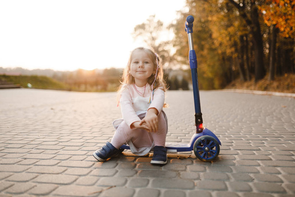 Usmívající se holčička sedí na skútru v parku a hledá rovně - Fotografie, Obrázek