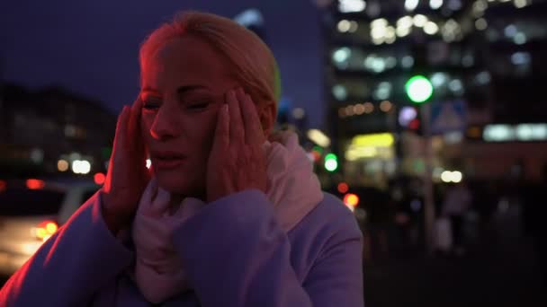 Dama de 50 años sufriendo de fuerte dolor de cabeza en el fondo de la ciudad de la noche
 - Imágenes, Vídeo