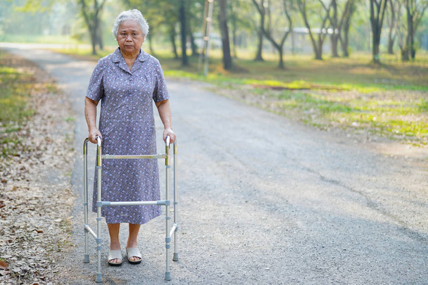 Aziatische senior of oudere oude dame patiënt lopen met walker in park: gezonde sterke medische concept  - Foto, afbeelding