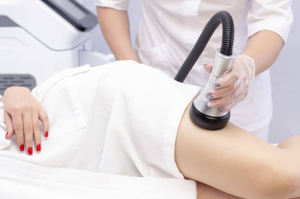 Cosmetologist reducing cellulite on the hips of a female patient, using ultrasound cavitation machine. Cropped shot of a woman getting rf lifting treatment on the back of her legs by professional beautician. - Φωτογραφία, εικόνα
