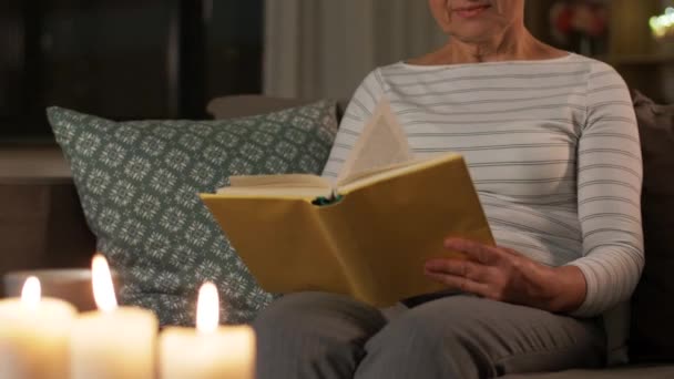 happy senior woman reading book at home in evening - Felvétel, videó