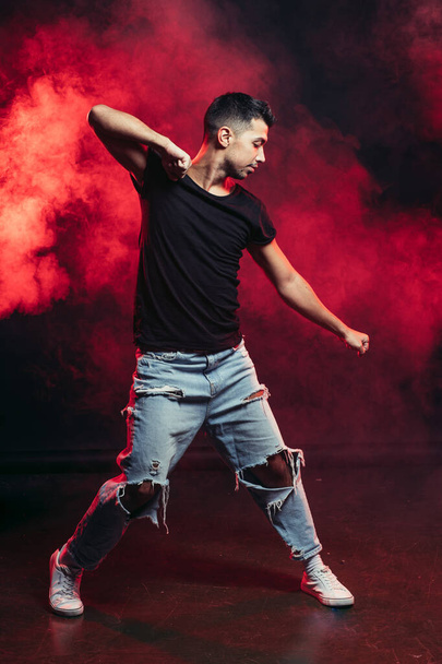dancing pose of young man on the dark red smoky background - Foto, imagen