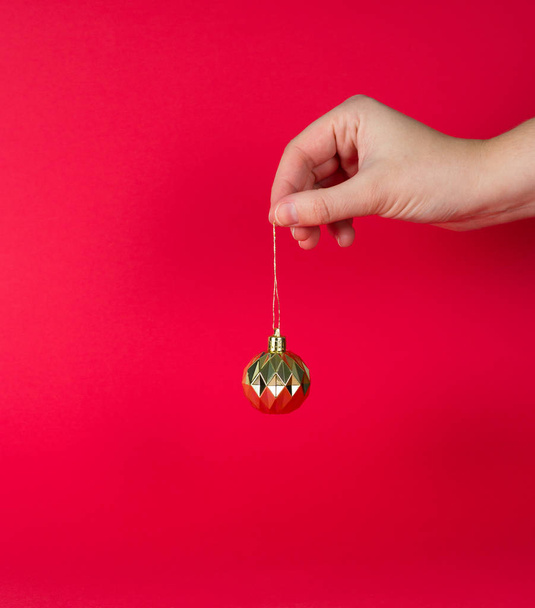 Christmas, new year mood on red background. Hand holds golden tree toy - Fotografie, Obrázek