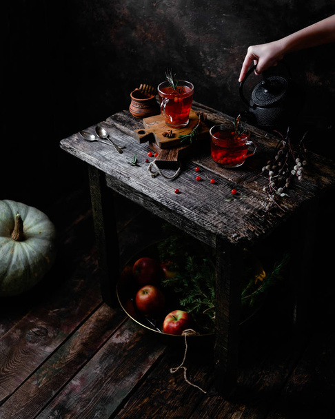 hand holding teapot and poring berry tea in glass cup on wooden table with berries and  apples with spruce branches and  - Foto, immagini