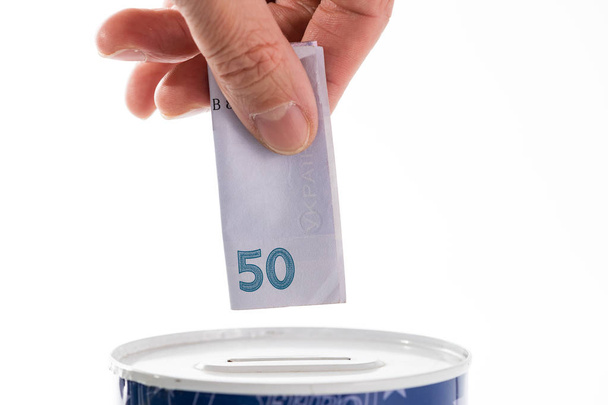 Hand putting bill into tin can saving bank - Photo, Image