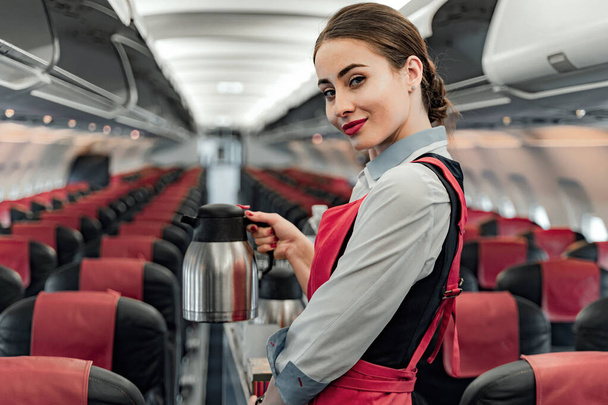 Nice young air hostess is standing in cabin - Photo, image