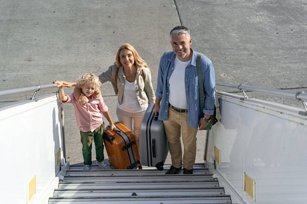 Ευτυχισμένη οικογένεια σκαρφαλώνει στη ράμπα του αεροπλάνου. - Φωτογραφία, εικόνα