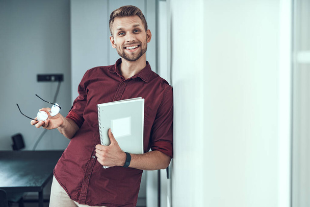 Smiling young man holding glasses in office - Foto, Bild