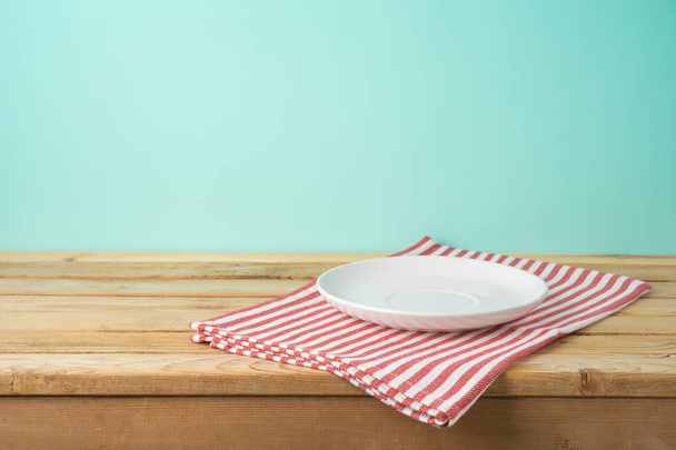 Wooden table with empty plate and tablecloth over blue backgroun - 写真・画像