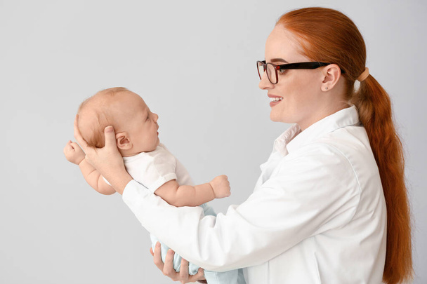 Pediatrician with cute baby on light background - Photo, Image