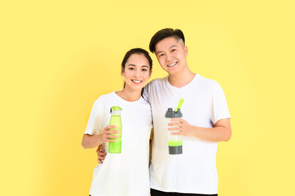 Sportief jong aziatisch paar met flessen water op kleur achtergrond - Foto, afbeelding