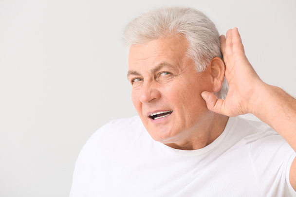 Mature man with hearing problem on light background - Foto, immagini