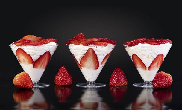 Strawberries with cream in cup on black background - Fotó, kép