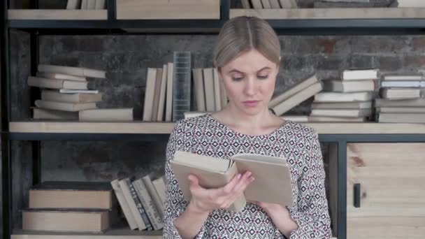 Retrato de la joven mujer bonita pasando páginas del viejo libro mientras estaba de pie entre los estantes de los libros en la biblioteca. De cerca. De interior
 - Metraje, vídeo