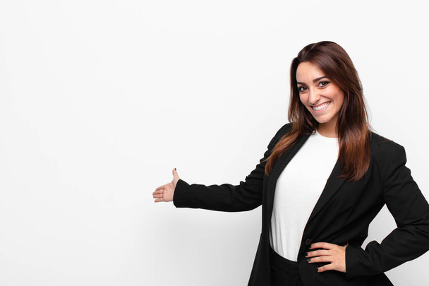 young pretty businesswoman feeling happy and cheerful, smiling and welcoming you, inviting you in with a friendly gesture against white wall - Photo, image