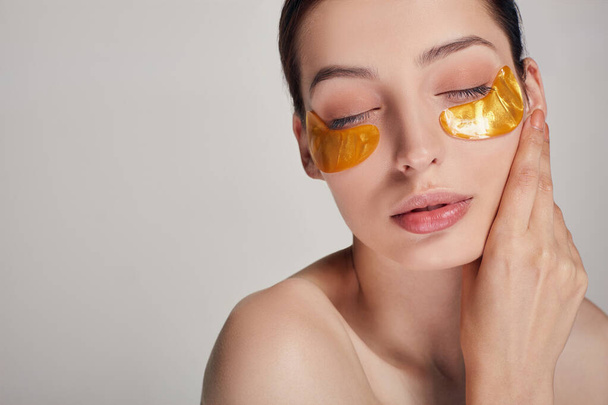 Young lovely girl applying golden collagen patches under her eyes - Foto, Imagem