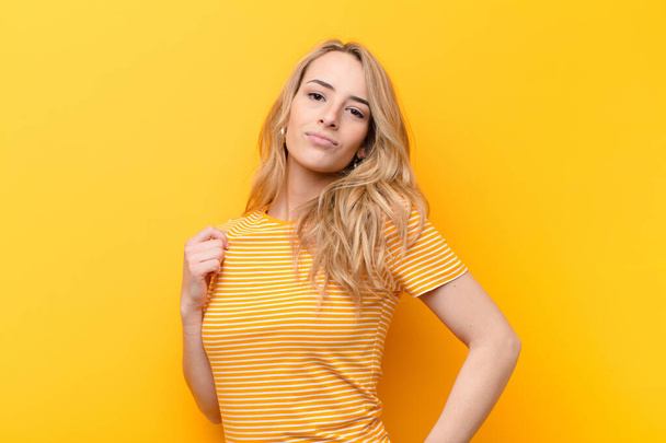 young pretty blonde woman looking arrogant, successful, positive and proud, pointing to self against flat color wall - Foto, imagen