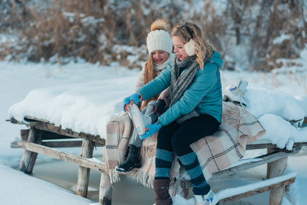 Familia se sienta en un banco en la orilla de un lago congelado
. - Foto, Imagen