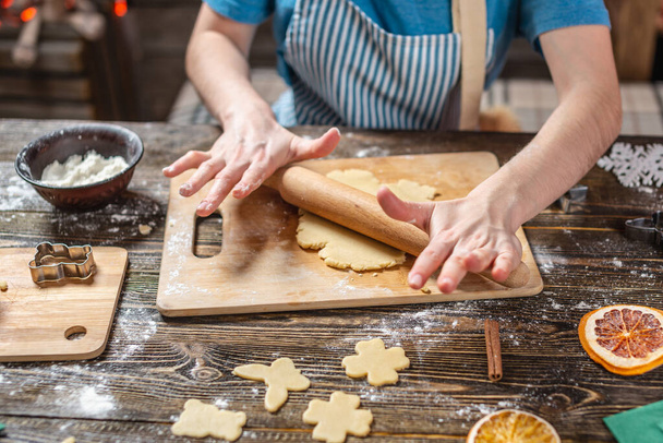 Woman rolls out the dough with a rolling pin and shapes festive gingerbread. Christmas time cooking delicious cookies. - Photo, Image