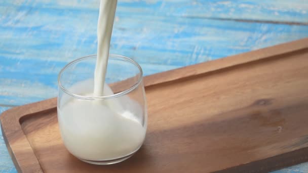 Ένα μπουκάλι γάλα και ένα ποτήρι γάλα σε ένα μπλε ξύλινο τραπέζι, υγιεινή γαλακτοκομικά προϊόντα έννοια - Πλάνα, βίντεο