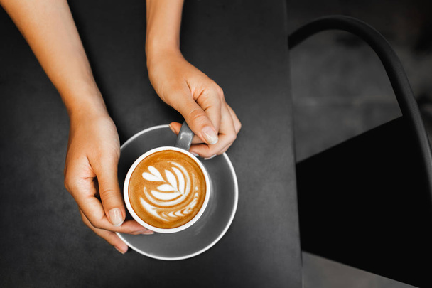 Coupe de cappuccino frais dans les mains de la femme sur la table en métal noir foncé
 - Photo, image