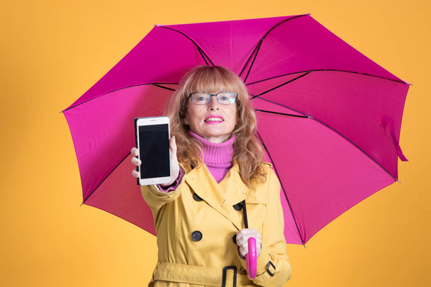adult woman with umbrella and mobile phone isolated on color background - Foto, afbeelding