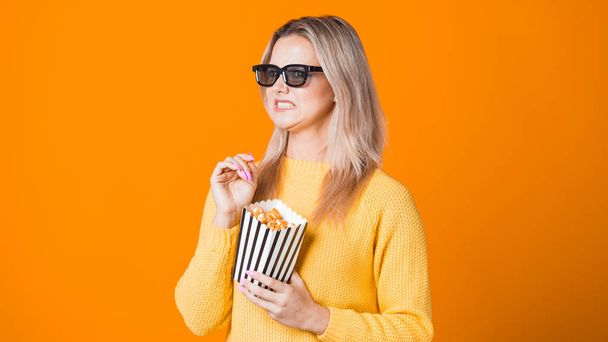 Young cheerful woman in 3D glasses watching a movie and eating popcorn. - Фото, изображение