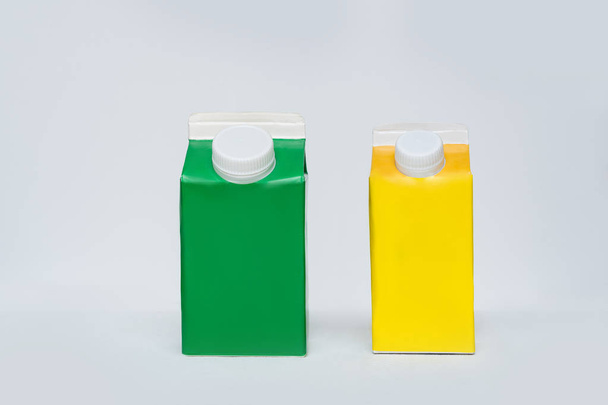 grüner und gelber Karton oder Verpackung der Tetrapackung mit Kappe auf weißem Hintergrund. - Foto, Bild