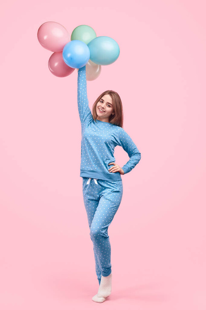 Joyful teen girl in pajamas carrying colourful balloons - Fotó, kép