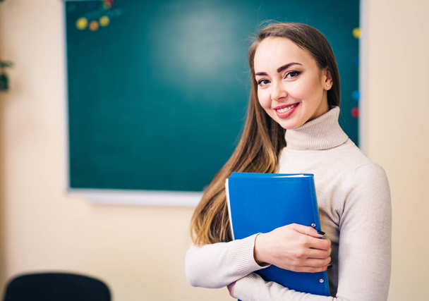 Attractive young woman teacher in a classroom teaching English language with notes in hands. - Foto, afbeelding