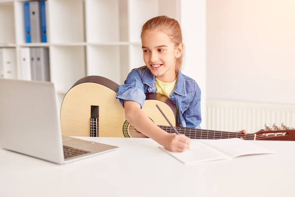 Cheerful child making notes during online guitar lesson - Valokuva, kuva