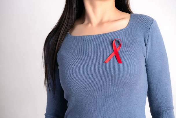 Primer plano de la cinta roja de la insignia en el pecho de la mujer para apoyar el Día del SIDA. Concepto de concienciación sobre salud, medicina y sida. - Foto, imagen
