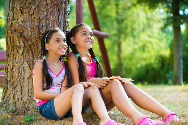 Hispanic sisters sitting under the tree and talking - Foto, Imagen