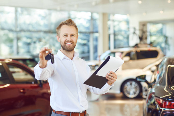 A car dealer holding a key in his hand in a showroom. - Foto, imagen