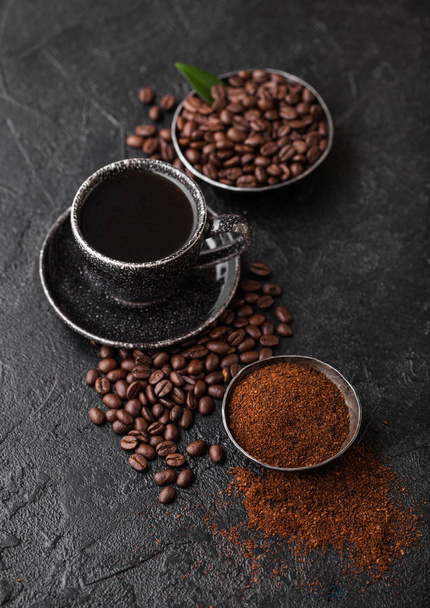 Cup of fresh raw organic coffee with beans and ground powder with cane sugar cubes with coffee tree leaf on black background. Top view - Foto, Imagem