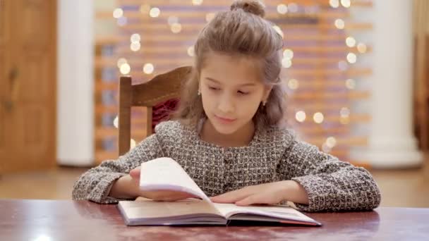 Mladá dívka listuje stránkami knihy a sní o dárcích na Nový rok. V pozadí, silvestrovská světla svítí. - Záběry, video