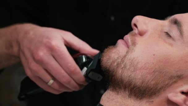 O barbeiro rapa a barba dos clientes numa cadeira. Corte de cabelo de barba. Barbeiro para barbear uma barba com uma navalha elétrica. Arrumação de homem real
 - Filmagem, Vídeo