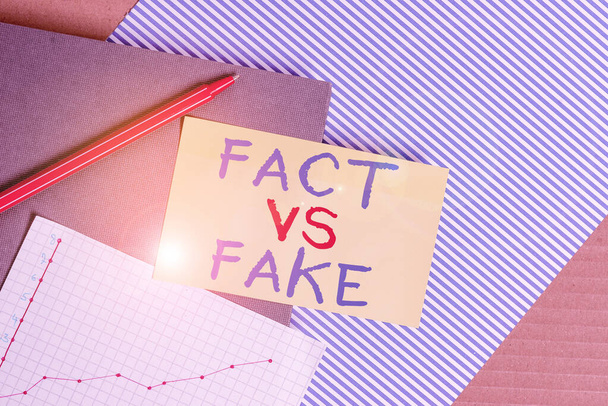 Conceptual hand writing showing Fact Vs Fake. Business photo showcasing Rivalry or products or information originaly made or imitation Striped paperboard cardboard office study supplies chart. - 写真・画像