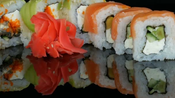 Různé barevné sushi rohlíky sad a zázvor na povrchu zrcadla na černém pozadí. Japonská kuchyně ve studiu - Záběry, video