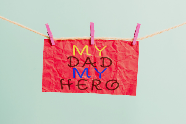 El yazısıyla "Kahramanım Babam" yazıyor. Kavram demek, babana duyulan hayranlık duygular çamaşır ipine, dikdörtgen şeklindeki kağıt hatırlatıcı beyaz ahşap masaya iltifat etmek demektir.. - Fotoğraf, Görsel