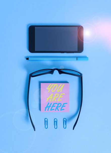 Word writing text You Are Here. Business concept for This is your location reference point global positioning system Dark eyeglasses colored sticky note smartphone pen clips pastel background. - Photo, Image
