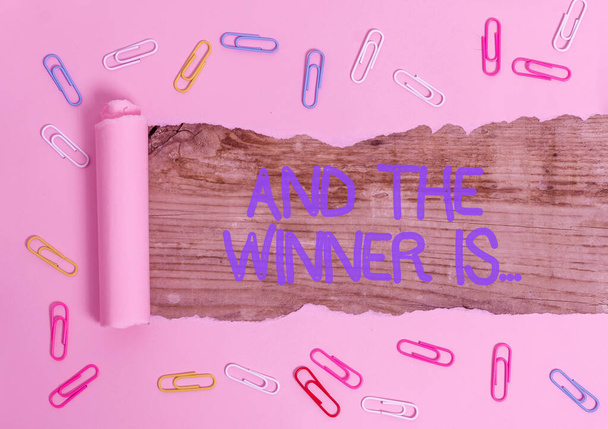 Handwriting text And The Winner Is. Concept meaning Announcing who the Victor is Exemplar Achiever Paper clip and torn cardboard placed above a wooden classic table backdrop. - Photo, Image