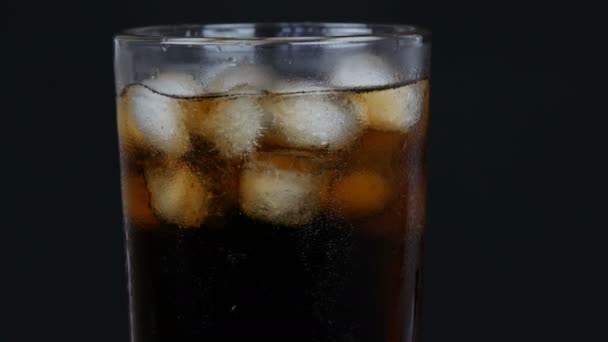 Burbujas de cola fría en un vaso largo transparente con hielo sobre un fondo negro
. - Metraje, vídeo