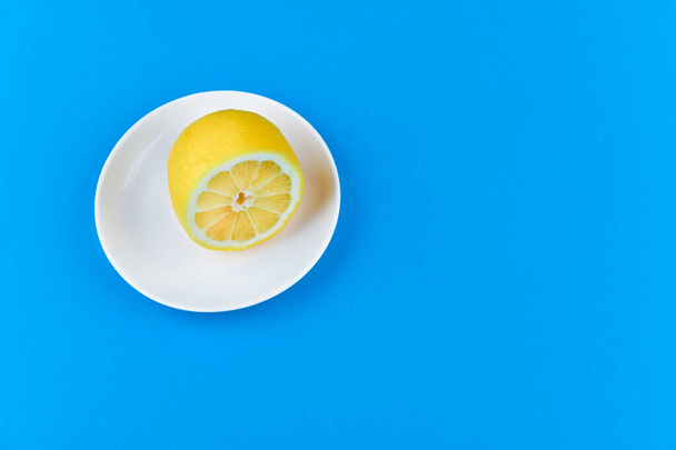 лимон на синем фоне. лежит на белой тарелке. наполовину лимон. Вид сверху. место для записи. Лимонные ломтики на синем фоне. Летом холодные ломтики апельсина. Лук, фрукты, перец, желток
 - Фото, изображение