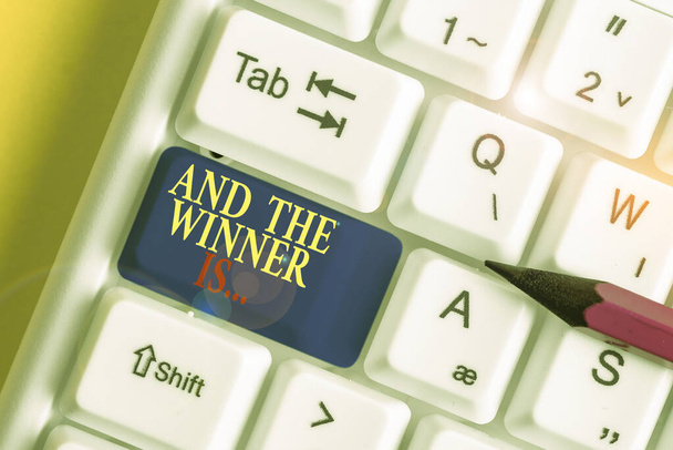 Handwriting text writing And The Winner Is. Concept meaning Announcing who the Victor is Exemplar Achiever White pc keyboard with empty note paper above white background key copy space. - Photo, Image