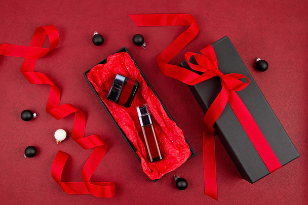 Woman's face care cosmetics packed in the black gift box with red ribbon over the red background - Foto, Imagem